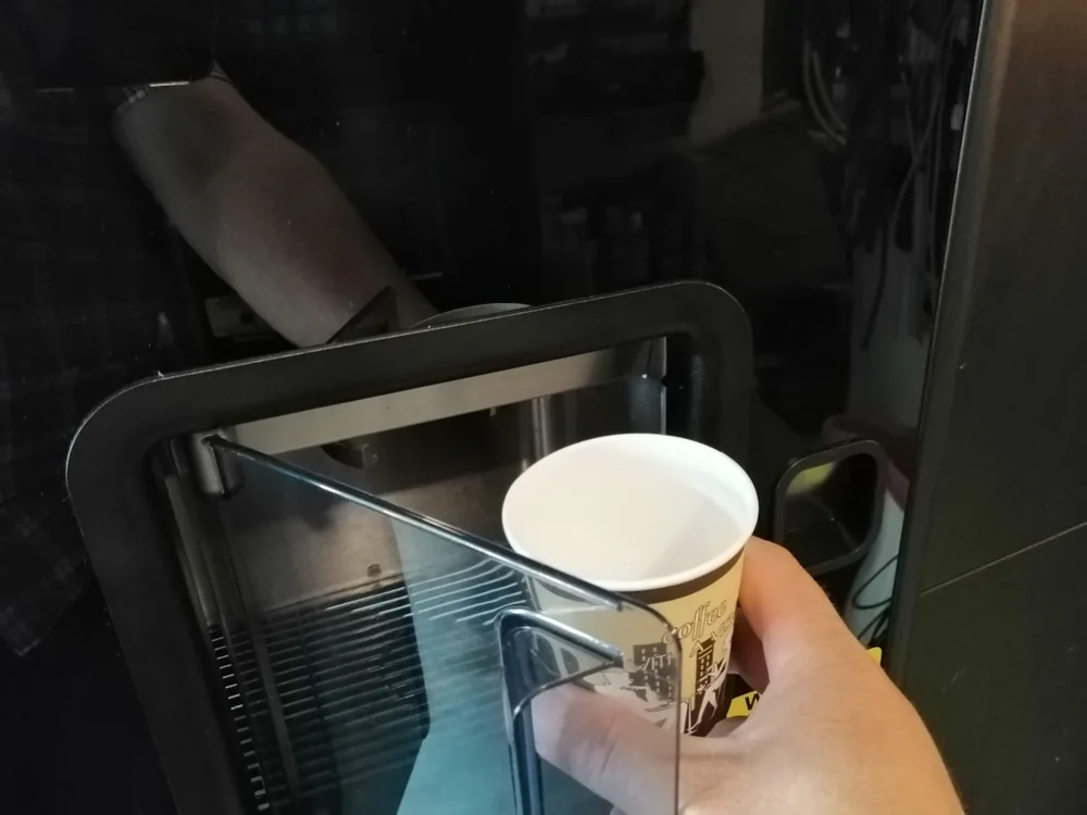 Un pahar de carton ținut în zona de dozare a unui automat de cafea
